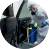a man in ppe kit spraying chemical in a car for infection from covid and other viruses