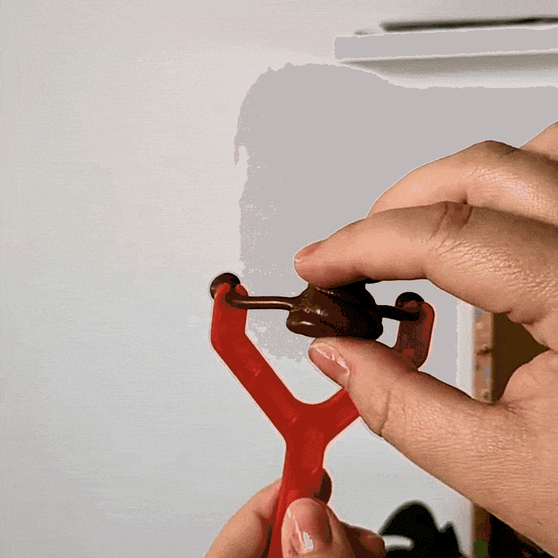 A hand pulls back a sticky poo toy in a catapult and fires it at the wall where it sticks