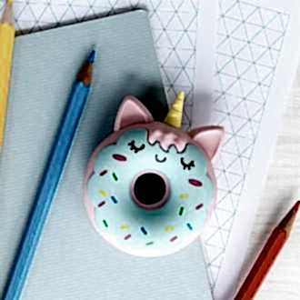 Doughnut-shaped unicorn eraser placed on a notebook beside coloured pencils.