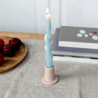 Taupe ceramic candle holder with a cylindrical shape and wide flat base, holding a lit candle