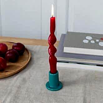 ceramic candle holder with a cylindrical shape and wide flat base, holding a lit red candle