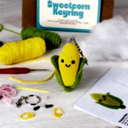 Crochet kit packaging displayed next to a finished yellow and green leaf sweetcorn keychain