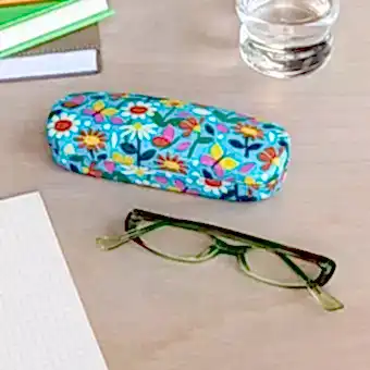 Light blue hardshell glasses case with print of butterflies amongst flowers on table