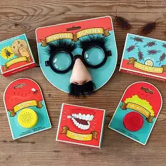 A selection of novelty toys including joke glasses with a nose and moustache, fake teeth, and other small trinkets, laid out on a wooden surface.