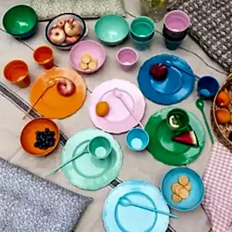 Bright melamine plates, bowls, cups, and cutlery arranged neatly on a patterned tablecloth, Ideal for picnic.