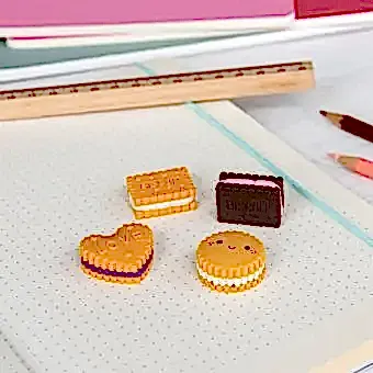 Four biscuit-shaped erasers in different styles and colours, placed on a notebook 
