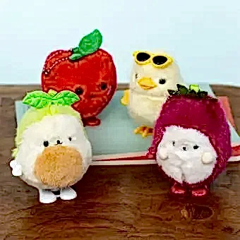 Four plush wind-up toys shaped like fruit and animals on a wooden surface