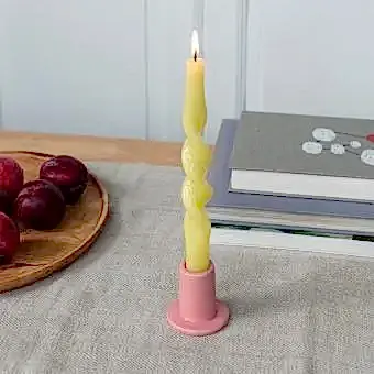 Pink ceramic candle holder with a cylindrical shape and wide flat base, holding a lit yellow candle