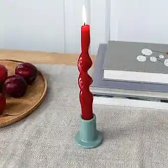 grey ceramic candle holder with a cylindrical shape and wide flat base, holding a lit red candle