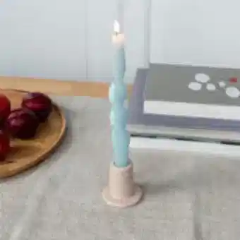 Taupe ceramic candle holder with a cylindrical shape and wide flat base, holding a lit candle