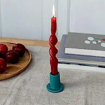 ceramic candle holder with a cylindrical shape and wide flat base, holding a lit red candle