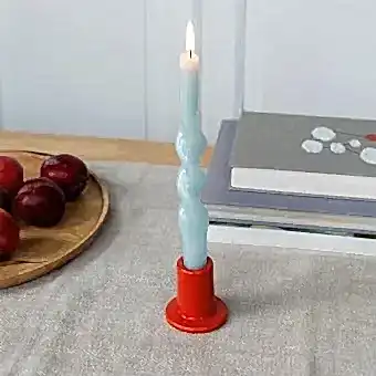 red ceramic candle holder with a cylindrical shape and wide flat base, holding a lit candle