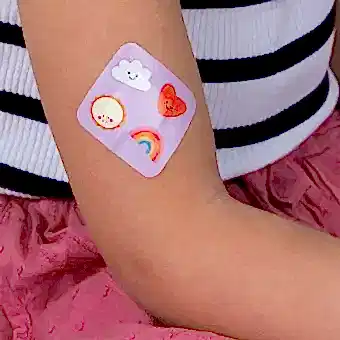 Plaster applied to a kid's arm with a kawaii sunshine-themed design.