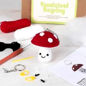Crochet kit packaging displayed next to a finished red and white toadstool mushroom keychain