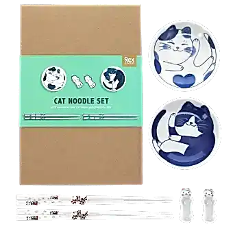 Two cat-themed dipping bowls, two pairs of chopsticks, and two cat-shaped rests beside a brown box.